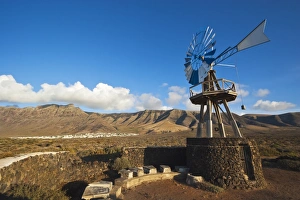 Traditional wind pump with 600m volcanic cliffs of the Risco de Famara rising over desert Traditional wind pump with 600m volcanic cliffs of the Risco de Famara rising over desert