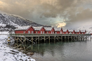 Typical red wooden huts of fishermen in the snowy and icy landscape of Lyngen Alps Typical red wooden huts of fishermen in the snowy and icy landscape of Lyngen Alps