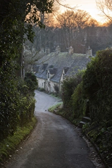 View down lane to Arlington Row Cotswold stone cottages at dawn, Bibury, Cotswolds View down lane to Arlington Row Cotswold stone cottages at dawn, Bibury, Cotswolds