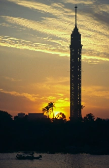 View at sunset of the Tower of Cairo and palm trees with small boat on River Nile in View at sunset of the Tower of Cairo and palm trees with small boat on River Nile in