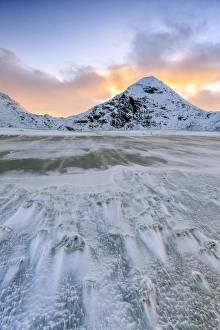 Wave advances towards the shore of the beach surrounded by snowy peaks at dawn, Uttakleiv Wave advances towards the shore of the beach surrounded by snowy peaks at dawn, Uttakleiv