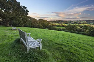 Wooden bench looking over green field countryside of High Weald on summer evening Wooden bench looking over green field countryside of High Weald on summer evening