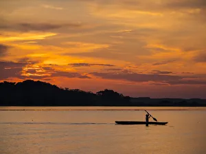 Young man paddling his fishing boat at sunset over calm waters on Clavero Lake, Amazon Young man paddling his fishing boat at sunset over calm waters on Clavero Lake, Amazon