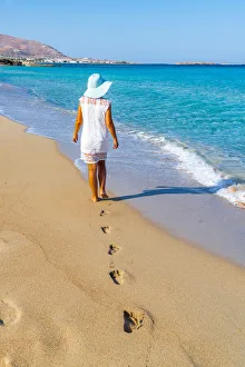 Young woman with sundress and hat walking on sand beach, Crete island, Greek Islands Young woman with sundress and hat walking on sand beach, Crete island, Greek Islands