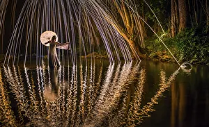 A young woman in a white dress standing in a river at night extends her hand to catch a A young woman in a white dress standing in a river at night extends her hand to catch a