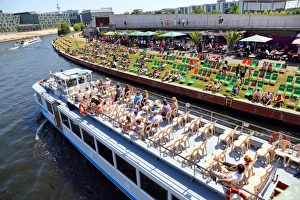 Artificial beach with deckchairs beside the River Spree with a tourist sightseeing boat Artificial beach with deckchairs beside the River Spree with a tourist sightseeing boat