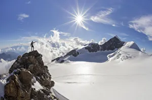 Alpinist over a rock near Balmenhorn bivac looking to Lyskamm peak with sun in backlight Alpinist over a rock near Balmenhorn bivac looking to Lyskamm peak with sun in backlight