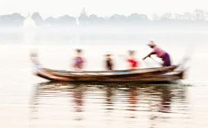 A boatman taking tourists in his traditional wooden boat across the Taungthaman Lake A boatman taking tourists in his traditional wooden boat across the Taungthaman Lake