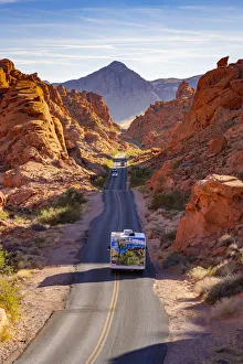 Campervan and cars driving on a straight road between red rocks during sunny day Campervan and cars driving on a straight road between red rocks during sunny day