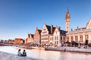 A couple of persons sitting by the water canal with Ghent waterfront building at sunset A couple of persons sitting by the water canal with Ghent waterfront building at sunset