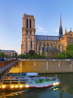 France, Paris, Notre Dame Cathedral and tour boat on River Seine at dusk