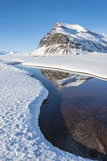 Iceland, Europe. Mountains mirroring in a crystal clear water surrounded by snow Iceland, Europe. Mountains mirroring in a crystal clear water surrounded by snow