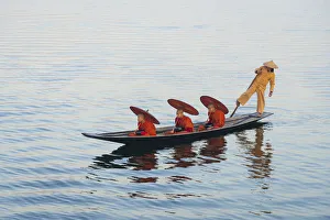 Three monks in orange robes with bowls for alms giving and a leg-rowing fisherman commute Three monks in orange robes with bowls for alms giving and a leg-rowing fisherman commute