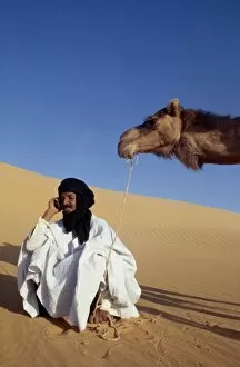A nomad sits in the desert and talks on his mobile phone
