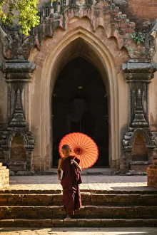 Novice Buddhist monk with red umbrella walking away from temple, Bagan, Mandalay Region Novice Buddhist monk with red umbrella walking away from temple, Bagan, Mandalay Region