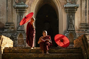 Two novice Buddhist monks with red umbrellas reading by temple, Bagan, Mandalay Region