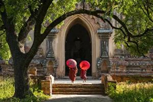 Two novice Buddhist monks with red umbrellas walking to temple, Bagan, Mandalay Region Two novice Buddhist monks with red umbrellas walking to temple, Bagan, Mandalay Region