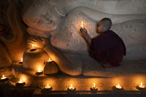 A novice monk holding a burning candle while praying by Buddha statue, UNESCO, Bagan A novice monk holding a burning candle while praying by Buddha statue, UNESCO, Bagan