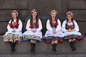 Poland, Cracow. Polish girls in traditional dress sitting at the base of the statue of Adam Mickiewicz, preparing to dance in Poland, Cracow. Polish girls in traditional dress sitting at the base of the statue of Adam Mickiewicz, preparing to dance in