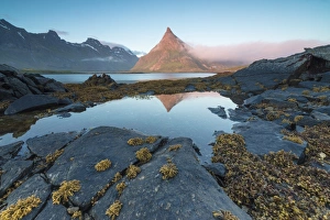 The rocky peak of Volanstinden lighted up by the midnight sun is reflected in blue The rocky peak of Volanstinden lighted up by the midnight sun is reflected in blue
