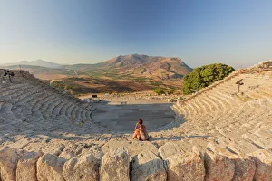 Segesta, Sicily. A woman sitting alone in the greek theater of Segesta at sunset Segesta, Sicily. A woman sitting alone in the greek theater of Segesta at sunset