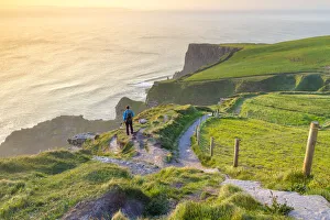 A tourist admiring the view of a sunset at the Cliffs of Moher A tourist admiring the view of a sunset at the Cliffs of Moher