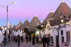 Tourist walks in the pedestrian area between trulli houses at twilight Tourist walks in the pedestrian area between trulli houses at twilight