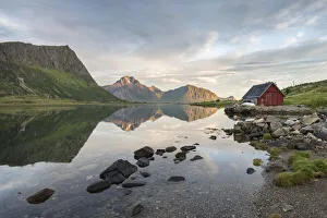 Typical rorbu and peaks reflected in the clear sea during midnight sun, Vengeren Typical rorbu and peaks reflected in the clear sea during midnight sun, Vengeren