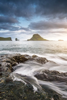 Vagar island, Faroe Islands, Denmark. Coastal rocks with Tinholmur islet at the background Vagar island, Faroe Islands, Denmark. Coastal rocks with Tinholmur islet at the background