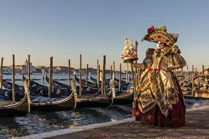 A woman in an elaborate costume poses in front of the Venice lagoon during the Venice A woman in an elaborate costume poses in front of the Venice lagoon during the Venice