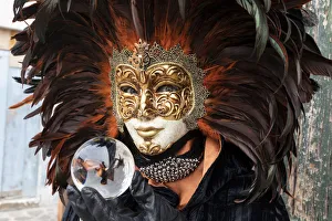 A woman in a feather Venetian mask poses with a glass ball during the Venice Carnival A woman in a feather Venetian mask poses with a glass ball during the Venice Carnival