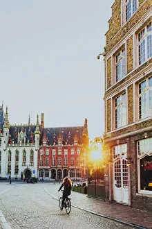 A woman riding a bike in Bruges Market Square at sunrise, Belgium A woman riding a bike in Bruges Market Square at sunrise, Belgium
