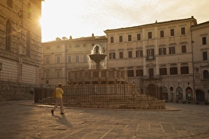 Woman walking past Fontana Maggiore in Piazza IV Novembre at dawn Perugia, Umbria, Italy Woman walking past Fontana Maggiore in Piazza IV Novembre at dawn Perugia, Umbria, Italy
