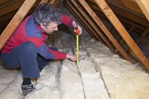 Global Warming Gallery: A man measuring the depth of insulation in a house loft or roof space