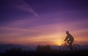 A man mountain biking at sunset on the Lake District hills, Cumbria, UK