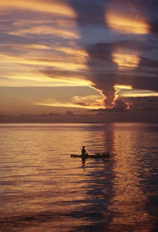 Person in canoe on sunset-orange lagoon.Papua New Guinea Person in canoe on sunset-orange lagoon.Papua New Guinea