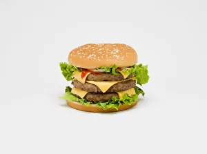 Food, Cooked, Meat Triple cheesburger with salad and tomato ketchup in a bun on a white Food, Cooked, Meat Triple cheesburger with salad and tomato ketchup in a bun on a white