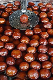 Indian fried sweet doughnuts in cooking pot of oil and syrup with single doughnut lifted out on spoon to drain Indian fried sweet doughnuts in cooking pot of oil and syrup with single doughnut lifted out on spoon to drain