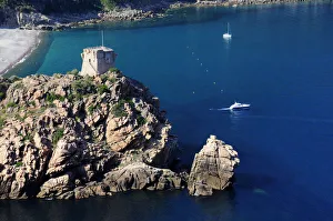 Porto Genoese tower on rocky headland with blue waters & boats Porto Genoese tower on rocky headland with blue waters & boats