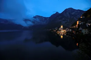 The alpine village of Hallstatt glows at dusk on the banks of Hallstaettersee lake in The alpine village of Hallstatt glows at dusk on the banks of Hallstaettersee lake in