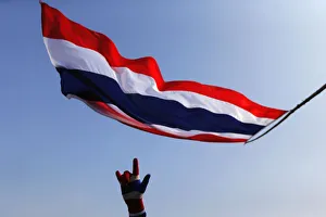 An anti-government protester gestures below a Thai national flag as he stands on a An anti-government protester gestures below a Thai national flag as he stands on a