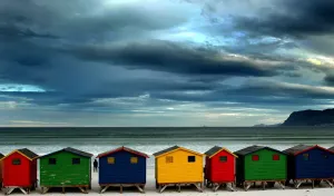 Cape Town Prints: Print of a stroller standing alone by beach huts at Muizenberg in Cape Town