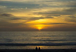 A couple sit on the sand watching the sun set on the Pacific Ocean in Cardiff A couple sit on the sand watching the sun set on the Pacific Ocean in Cardiff