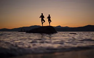 A couple stand on a rock facing the sunset along the shores of English Bay in Vancouver A couple stand on a rock facing the sunset along the shores of English Bay in Vancouver