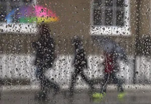 Family is seen through raindrops on a window as they shelter under umbrellas during a Family is seen through raindrops on a window as they shelter under umbrellas during a