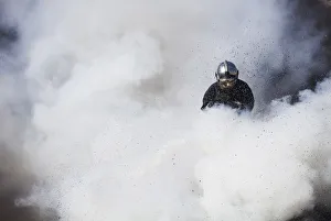 A firefighter is engulfed by white smoke while extinguishing burning tyres during A firefighter is engulfed by white smoke while extinguishing burning tyres during