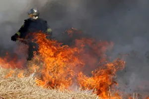 A French fireman uses a shovel behind flames in a burning field of barley during harvest A French fireman uses a shovel behind flames in a burning field of barley during harvest