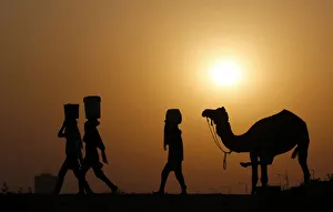 Girls carrying buckets filled with water are silhouetted against the setting sun as Girls carrying buckets filled with water are silhouetted against the setting sun as