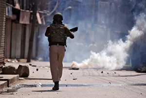 An Indian policeman chases protesters amid tear gas smoke during a protest after An Indian policeman chases protesters amid tear gas smoke during a protest after