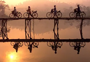 Indonesian villagers push their bicycles across a bamboo bridge as sun rises behind them Indonesian villagers push their bicycles across a bamboo bridge as sun rises behind them